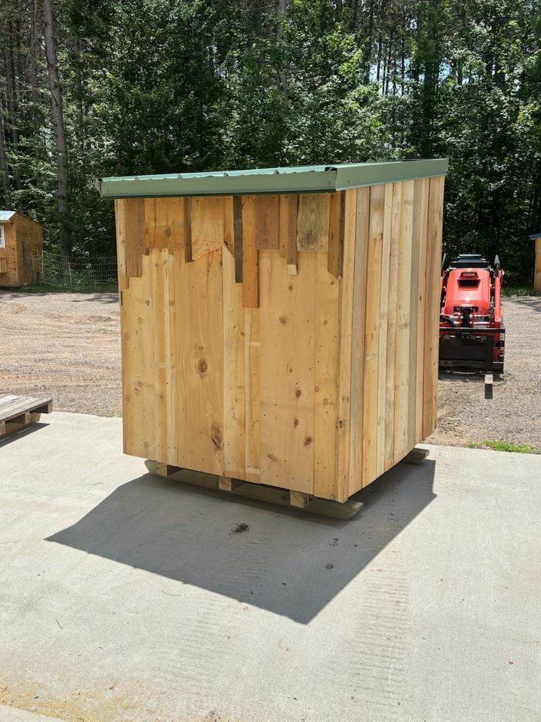 Back of a small green-roofed shed on a concrete pad