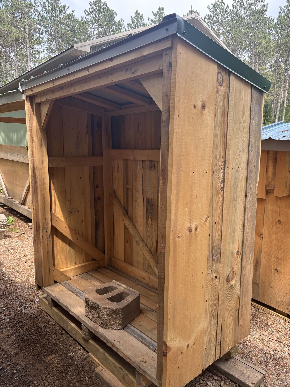 Tall, narrow firewood shed with a green roof and rough-sawn siding