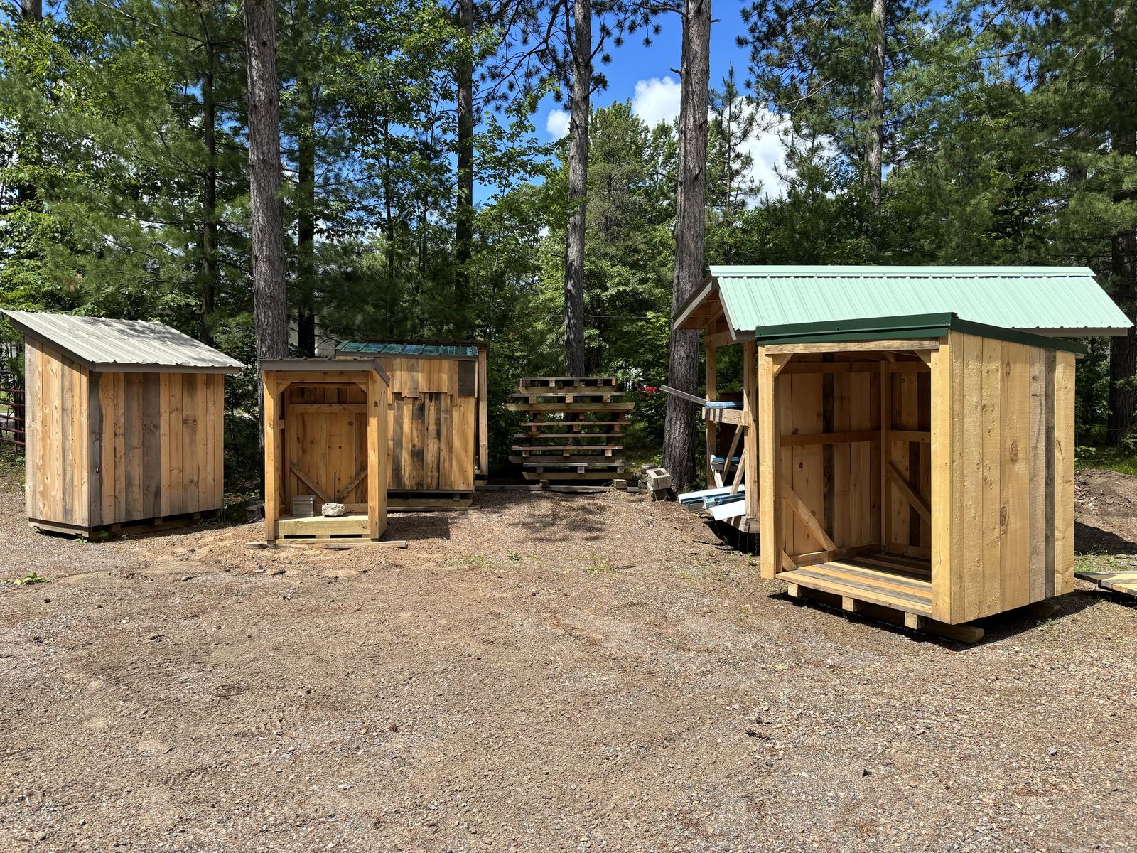 Four finished sheds lined up in a gravel yard under pines